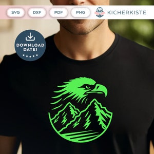 Peut inclure: T-shirt noir avec un motif vert néon représentant une tête d'aigle et des montagnes dans un cercle. Le design est centré sur le t-shirt. Le texte "DOWNLOAD DATEI" est sur un badge circulaire bleu.
