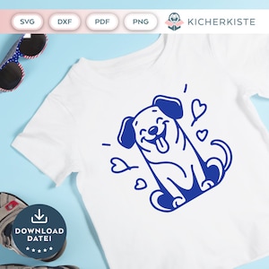 Op de afbeelding: Een wit T-shirt met een blauw cartoon-hondontwerp. De hond glimlacht en heeft zijn tong uitgestoken. Er zijn hartjes rond de hond.
