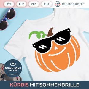 Op de afbeelding: Een wit T-shirt met een oranje pompoen die een zwarte zonnebril draagt. De pompoen heeft een groene steel en een glimlachend gezicht. De tekst "Kürbis mit Sonnenbrille" staat onderaan het shirt.