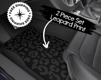 May include: Two black car floor mats with a leopard print design. The mats are in the front passenger and driver's side of a car. The text "2 Piece Set Leopard Print" is written in white on a black background.