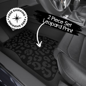 May include: Two black car floor mats with a leopard print design. The mats are in the front passenger and driver's side of a car. The text "2 Piece Set Leopard Print" is written in white on a black background.