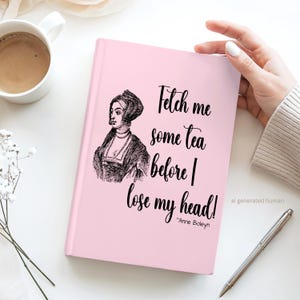 May include: A light pink hardcover journal featuring a black ink illustration of Anne Boleyn and the text "Fetch me some tea before I lose my head! ~Anne Boleyn" printed in a decorative script font on the front cover.