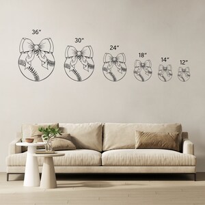May include: Six different sizes of baseball-shaped wall decor with a bow on top. The sizes are 36 inches, 30 inches, 24 inches, 18 inches, 14 inches, and 12 inches. The decor is shown on a white wall with a beige couch and two white side tables.