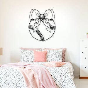 May include: A black and white illustration of a baseball with a large bow on top. The illustration is on a white wall above a bed with pink and white polka dot bedding.