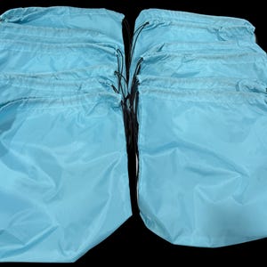 May include: A collection of light blue drawstring bags. Each bag is made of a smooth, slightly shiny material and has a black drawstring closure. The bags are arranged in two groups against a black background, suggesting they are for storage or travel.