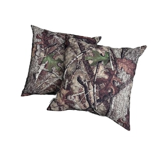 May include: Two square throw pillows with a camouflage pattern in shades of brown, green, and white. The pattern resembles tree branches and leaves.