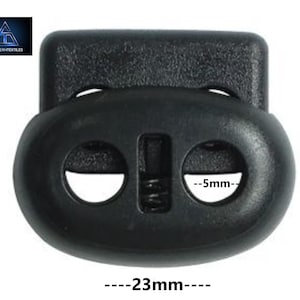 May include: Black plastic toggle buckle with two holes, measuring 20 mm in height and 23 mm in width. The buckle has a 5 mm wide opening for a cord or strap.