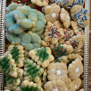 May include: A silver tray filled with an assortment of decorated cookies. The cookies are various shapes, including flowers, trees, and circles, and are adorned with colorful sprinkles and sugar crystals. Some cookies have green, red, and white sprinkles, while others have blue sprinkles.