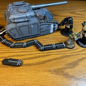 Puede incluir: Un tanque en miniatura gris y negro con una oruga negra y blanca, una flecha negra y blanca y tres figuras en miniatura negras y blancas.