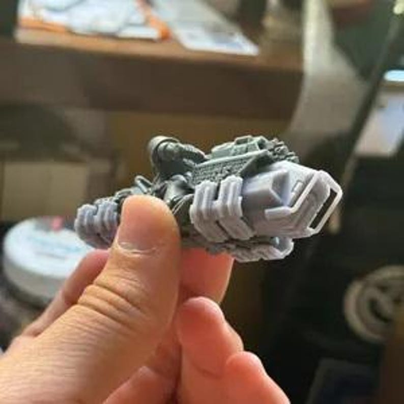 Puede incluir: Un peque&ntilde;o modelo gris impreso en 3D de un veh&iacute;culo futurista, sostenido en la mano de una persona. El veh&iacute;culo tiene un dise&ntilde;o detallado con m&uacute;ltiples componentes, incluyendo una cabina y elementos mec&aacute;nicos. El modelo mide aproximadamente 10 cm de largo.