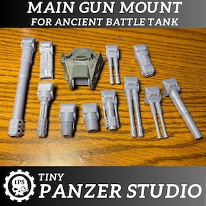 May include: A selection of grey 3D-printed miniature tank components, including gun barrels, turrets, and mounts. The text at the top reads "MAIN GUN MOUNT FOR ANCIENT BATTLE TANK." The Tiny Panzer Studio logo is at the bottom.