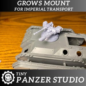 May include: A gray plastic model of a twin heavy bolter turret, designed to be mounted on a miniature Imperial Transport vehicle. The turret is labeled "GROWS MOUNT FOR IMPERIAL TRANSPORT" and "TINY PANZER STUDIO".