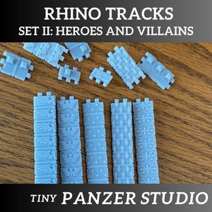 May include: Light blue Rhino Tracks set, featuring various track designs. The text "RHINO TRACKS SET II: HEROES AND VILLAINS" and "TINY PANZER STUDIO" are visible. The tracks are arranged on a wooden surface.
