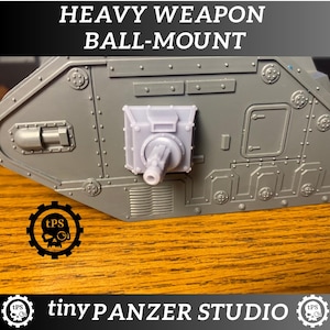 May include: A gray plastic model of a tank with a heavy weapon ball-mount. The text "HEAVY WEAPON BALL-MOUNT" is at the top. The logo for "tinyPANZER STUDIO" is at the bottom.