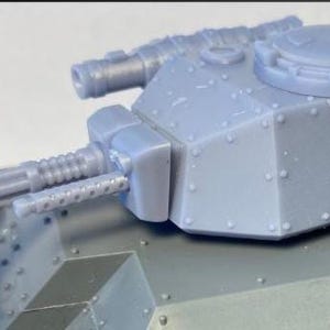 May include: A detailed, light gray model of a tank turret. The turret features a main gun, a smaller machine gun, and various hatches and details. The model is made of a solid, possibly plastic, material and is designed for hobbyists.