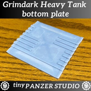 Puede incluir: Placa inferior de tanque pesado Grimdark azul claro. La placa rectangular presenta una serie de líneas paralelas y detalles cuadrados. El texto "Grimdark Heavy Tank bottom plate" y "tinyPANZER STUDIO" es visible.