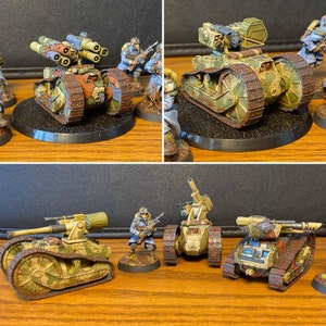 Puede incluir: Un conjunto de cinco figuras de juego de guerra en miniatura, que incluyen cuatro soldados y un tanque. El tanque está pintado con un patrón de camuflaje marrón, verde y tostado. Los soldados están pintados con uniformes azules y grises. Las figuras están dispuestas en una escena de batalla.