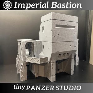 May include: A gray, 3D-printed Imperial Bastion model. The model features a multi-level structure with detailed architectural elements, including windows, a balcony, and textured surfaces. The text "Imperial Bastion" and "tinyPANZER STUDIO" are visible.