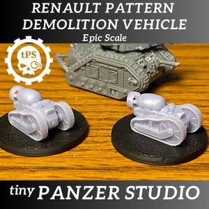 May include: Two grey plastic miniature tank models on black bases. The tanks have a rounded front and a long barrel. The tanks are labelled "Renault Pattern Demolition Vehicle Epic Scale".