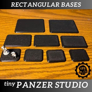 Puede incluir: Un conjunto de nueve bases rectangulares negras para figuras en miniatura. Las bases están hechas de un material texturizado y están dispuestas en un patrón de cuadrícula sobre una superficie de madera. Las bases están etiquetadas como "RECTANGULAR BASES" y "tiny PANZER STUDIO".