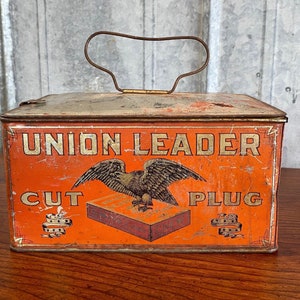 May include: Vintage orange metal tin with a handle. The tin has a label that says "Union Leader Cut Plug" with an eagle graphic.