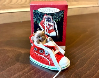 May include: A Hallmark Keepsake Ornament of a brown hedgehog in a red trainer with white laces. The trainer has a white toe cap and green trim. A matching image is on the red box behind the ornament.