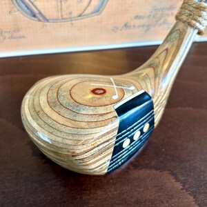 Puede incluir: Un palo de golf de madera vintage con una cabeza marr&oacute;n claro y un acento azul oscuro. El eje del palo es plateado y el agarre est&aacute; envuelto con hilo. La cabeza presenta una marca blanca y tres peque&ntilde;os puntos blancos.