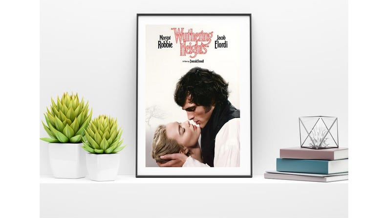 Puede incluir: Un p&oacute;ster enmarcado de la pel&iacute;cula "Cumbres Borrascosas" con Margot Robbie y Jacob Elordi. El p&oacute;ster muestra un primer plano de los actores bes&aacute;ndose. Dos plantas suculentas verdes en macetas blancas y una pila de libros en una estanter&iacute;a blanca.