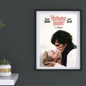 Puede incluir: P&oacute;ster enmarcado de la pel&iacute;cula "Cumbres Borrascosas" con Margot Robbie y Jacob Elordi. El p&oacute;ster muestra un primer plano de los actores en un abrazo rom&aacute;ntico. El p&oacute;ster est&aacute; en un marco negro y cuelga de una pared gris oscura.