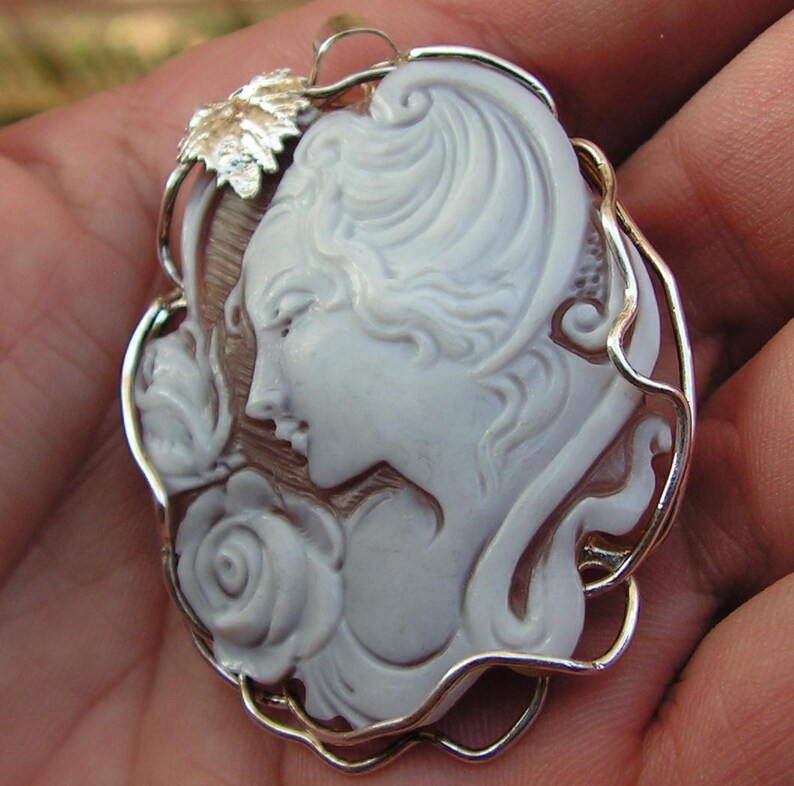 May include: A white cameo pendant featuring a woman's profile with a rose, set in a silver-toned wire frame.