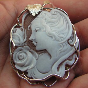 May include: A cameo pendant featuring a woman's profile with a rose, carved from white shell and set in a silver filigree frame.