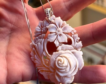 Può includere: Una collana con pendente floreale con un pendente scolpito bianco sporco, con un design a rosa e altri fiori. Il pendente è sospeso a una delicata catena d'argento. Il pendente è lungo circa 5 cm.