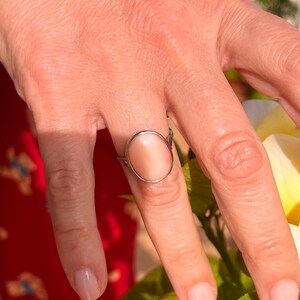 K&ouml;nnte beinhalten: Ein silberner Ring mit einem ovalen, pfirsichfarbenen Stein. Der Ring hat ein schlichtes, elegantes Design und wird an einem Finger getragen. Der Hintergrund zeigt ein rotes Blumenmuster und gr&uuml;ne Bl&auml;tter.