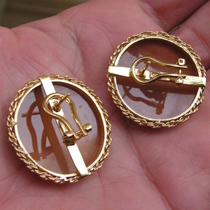 May include: A pair of gold tone clip-on earrings with a brown stone set in a rope-like design.