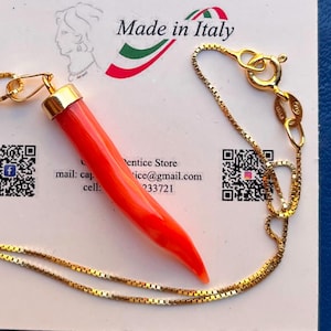 Könnte beinhalten: Eine goldene Kastenketten-Halskette mit einem leuchtend orangefarbenen, hornförmigen Anhänger mit goldener Kappe. Die Kette hat einen Federringverschluss und ein kleines Plättchen mit der Prägung 925, präsentiert auf einer Karte mit Made in Italy.