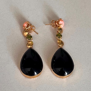 May include: A pair of gold drop earrings. Each earring has a black, teardrop-shaped stone with a gold rim, and a series of smaller green and gold stones, topped with a pink stone. The earrings are for pierced ears.