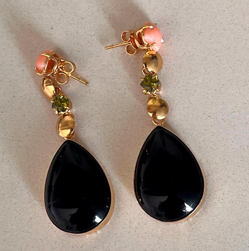 May include: A pair of gold-coloured drop earrings. Each earring features a black teardrop-shaped stone, accented with pink, green, and gold-coloured beads. The earrings have a post-back closure.