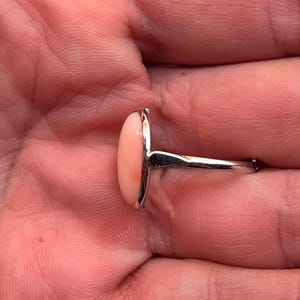 K&ouml;nnte beinhalten: Ein Silberring mit einem gro&szlig;en, ovalen Korallenstein. Die Koralle hat einen weichen, pfirsichrosa Farbton mit einem nat&uuml;rlichen Muster. Der Ring hat ein poliertes Silberband und eine Fassung.