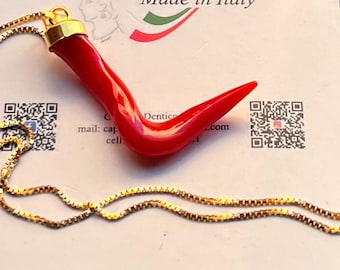 May include: A bright red, curved horn-shaped pendant with a gold-toned metal cap, suspended from a thin gold-toned box chain. The pendant rests on a white card featuring the text Made in Italy and two QR codes on the left and right sides.