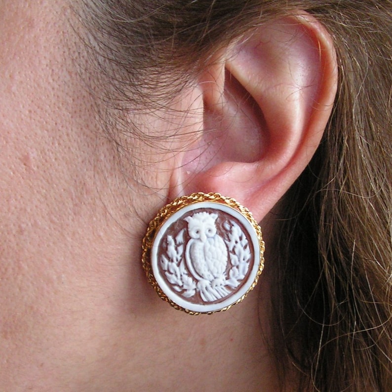 May include: A pair of gold-tone earrings with a brown cameo featuring a white owl design.