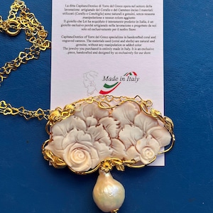 Puede incluir: Un collar dorado con un colgante con un dise&ntilde;o floral tallado y una gran perla en forma de pera. El colgante est&aacute; hecho de un material de color claro, posiblemente concha o coral, y est&aacute; acentuado con detalles dorados. El texto "Made in Italy" es visible.
