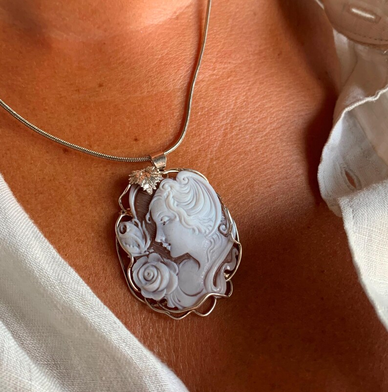 May include: A silver chain necklace with a cameo pendant featuring a woman's profile with a rose and a butterfly. The cameo is set in a silver frame.