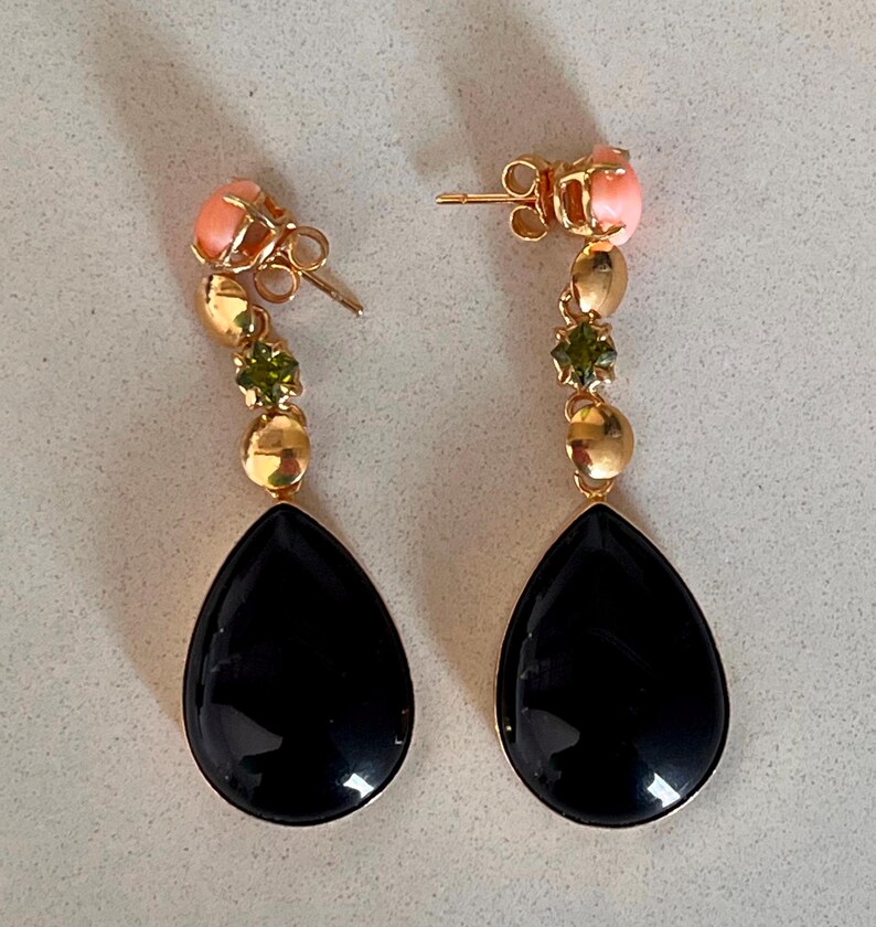 May include: A pair of gold drop earrings. Each earring has a black, teardrop-shaped stone, gold beads, green stones, and a pink coral-like stud.
