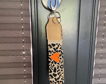 Colorful key fob made of light leopard print webbing, an orange heart and cream-colored leather end, carabiner + key ring