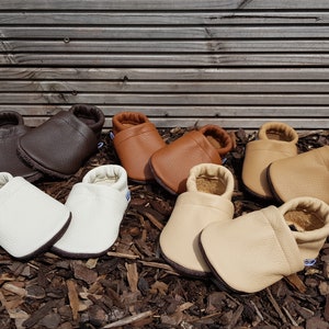 May include: Four pairs of soft-soled baby shoes in various shades of brown, tan, cream, and white. Each pair features a textured leather-like finish, a rounded toe, and an elasticized ankle opening for a secure fit on the feet.