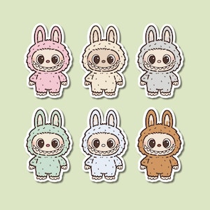 May include: Six cartoon stickers featuring a smiling monster in a bunny suit. The stickers are in various pastel colors: pink, beige, gray, mint green, light blue, and brown. Each sticker has a white border and a green background.