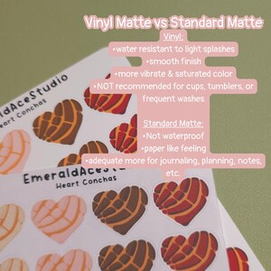 May include: Sticker sheets featuring heart-shaped concha designs in various colors. The text "Vinyl Matte vs Standard Matte" is displayed, along with descriptions of each finish. The stickers are from EmeraldAceStudio.