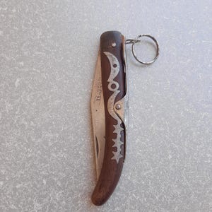 May include: A closed pocket knife with a dark brown wooden handle and a silver metal blade. The handle has decorative silver accents. A small metal ring is attached to the end of the knife.