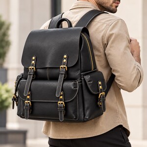 Puede incluir: Una mochila negra con una solapa superior grande, dos bolsillos delanteros y dos bolsillos laterales, todos asegurados con hebillas y remaches de metal en tono latón. La bolsa incluye correas ajustables para los hombros, un asa superior y costuras blancas visibles.