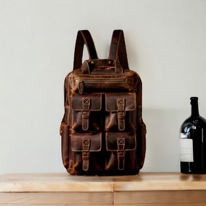 May include: A brown leather backpack with multiple pockets and buckles. The backpack has a distressed look and is made of high-quality leather.